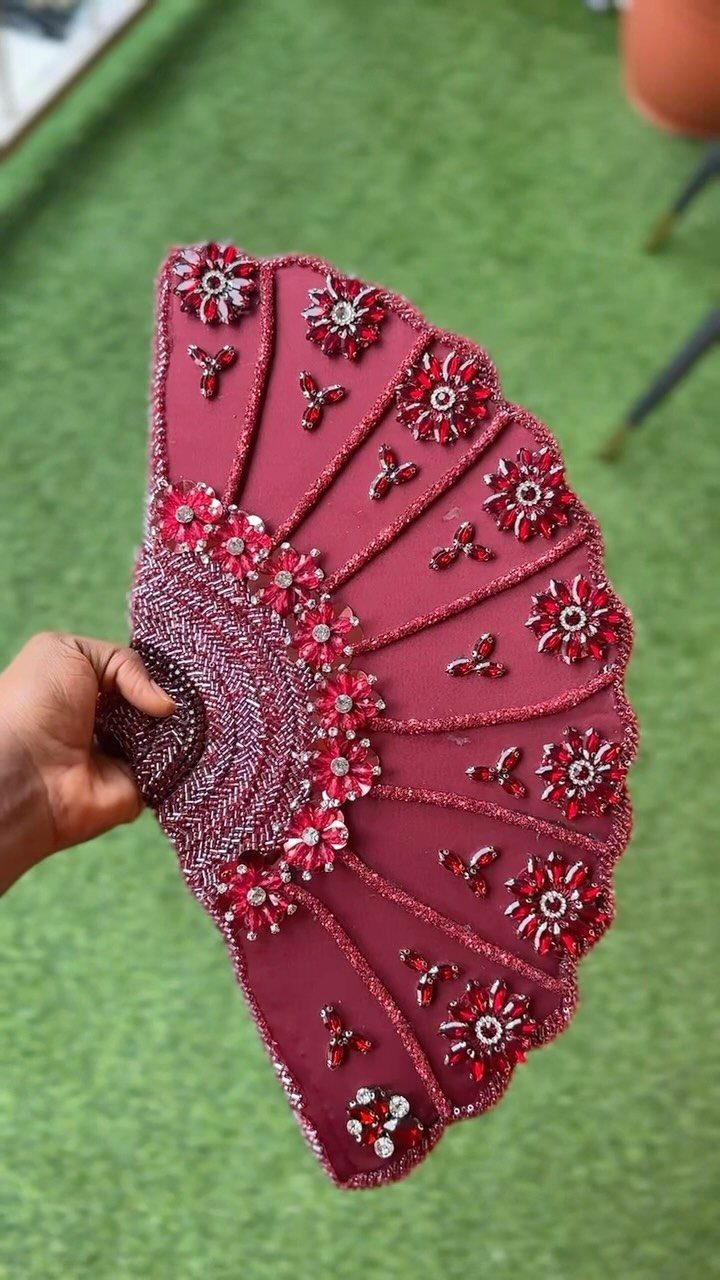 12 Wedding Bouquet Alternatives for Your Big Day 12 Burgundy handheld fan with red beads and rhinestones held against green grass.
