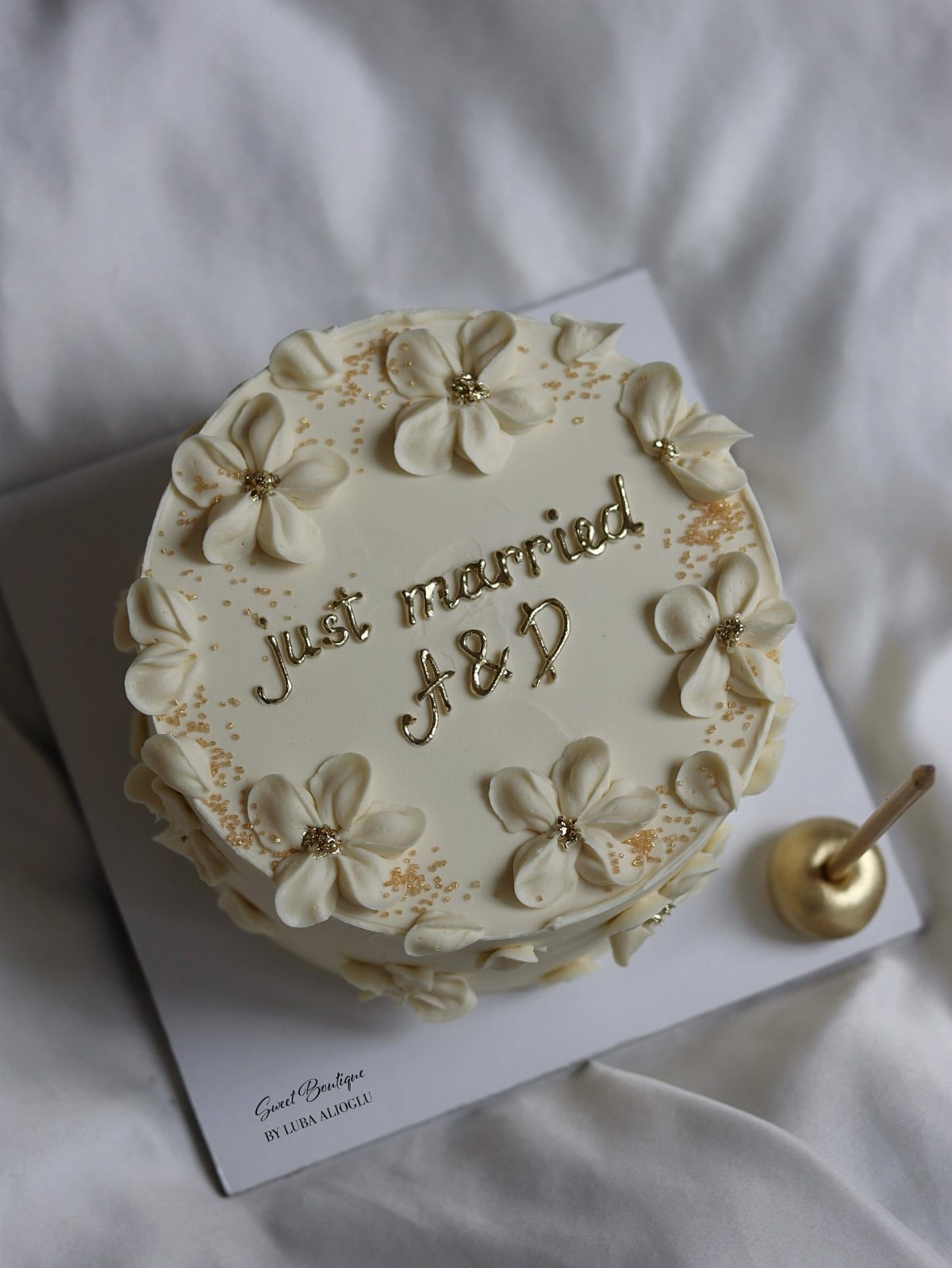 5 Wedding Cake Just Married Ideas for Real Budgets 3 A single-tier white frosted cake decorated with buttercream flowers and gold 'just married' script.