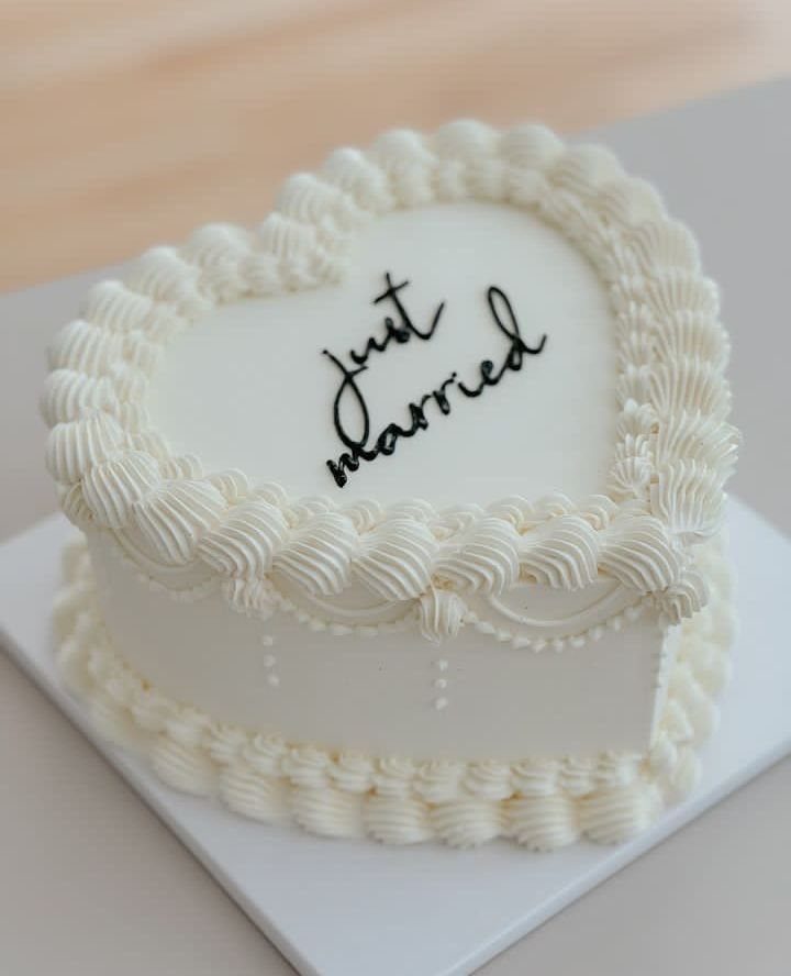 5 Wedding Cake Just Married Ideas for Real Budgets 2 A heart-shaped white buttercream cake with black cursive lettering that says just married.