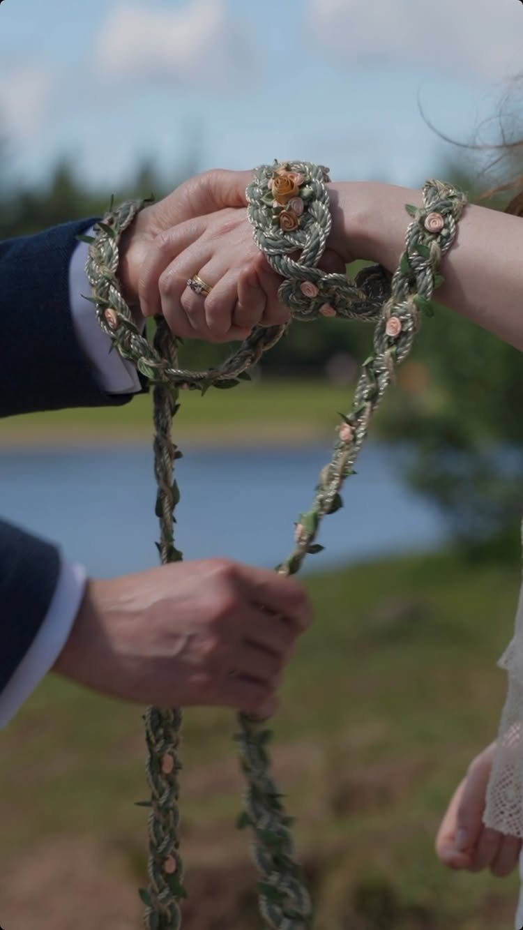 Hands of a couple bound together with a braided floral cord during handfasting.