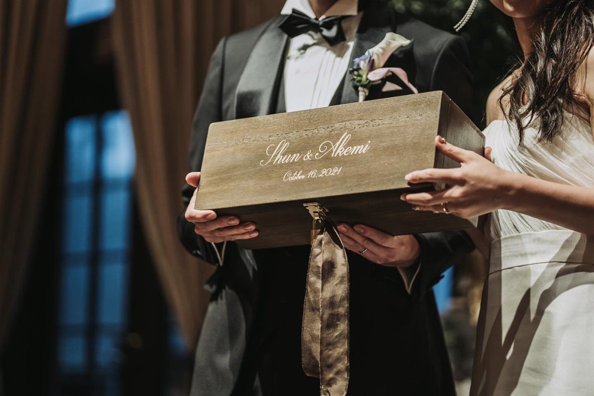 Couple in wedding attire holding an engraved wooden wine box tied with ribbon