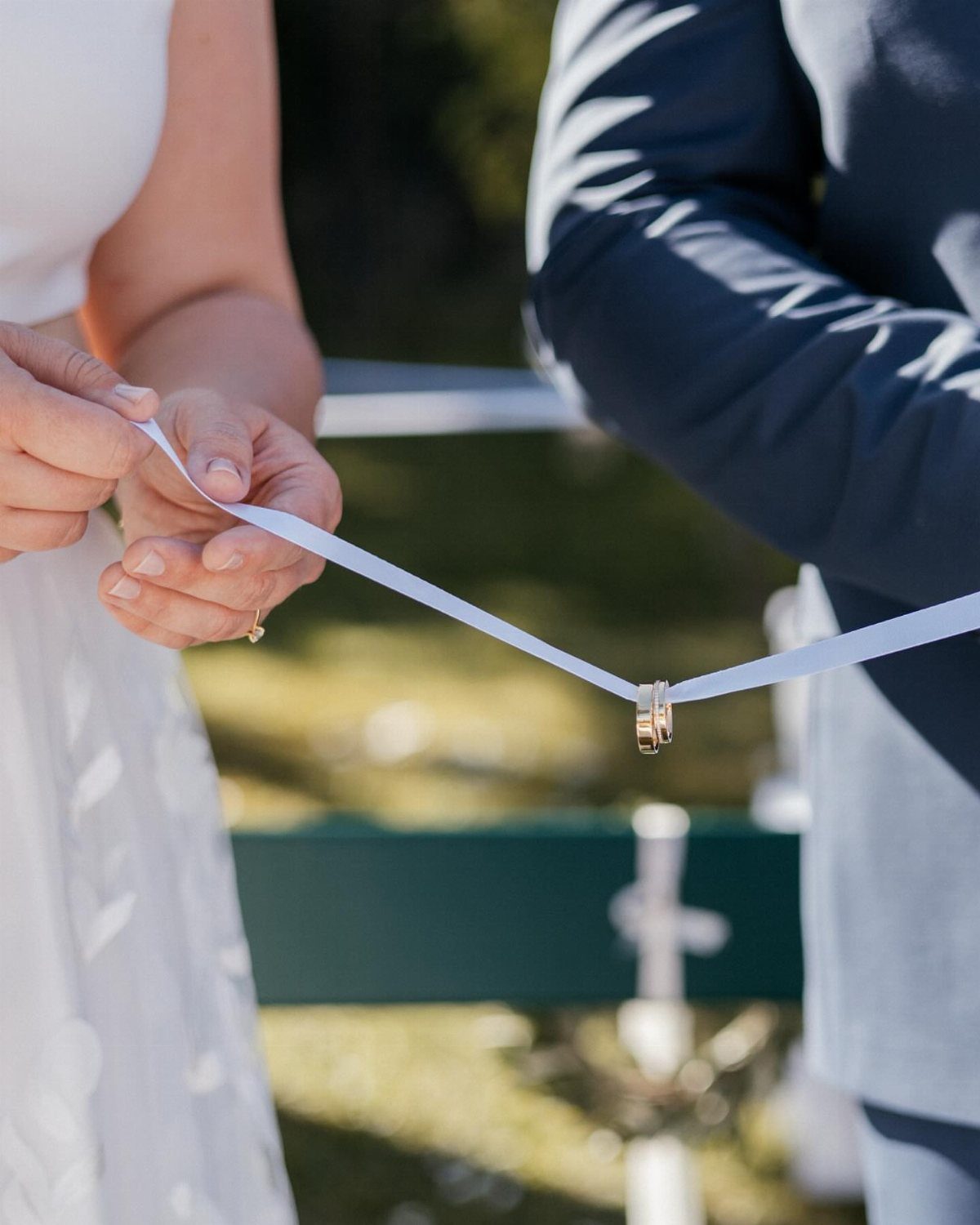 Wedding rings tied to a white ribbon held by a bride and groom.