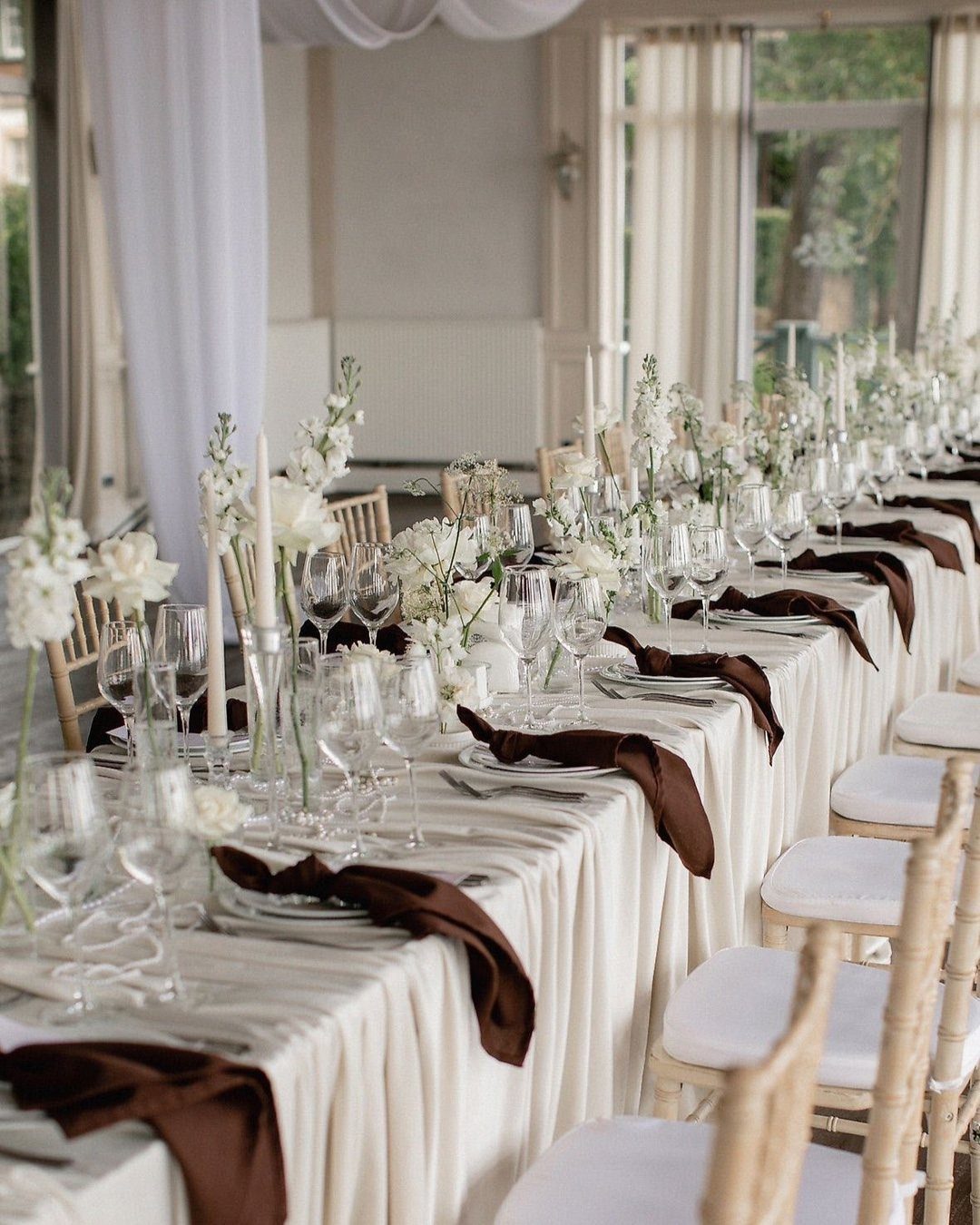 Wedding Decor Brown: How to Use It in 8 Elegant Ways 3 A long wedding table set with cream linens, brown satin napkins, and white flowers.