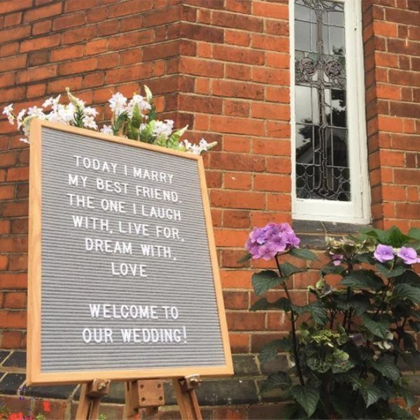 Wedding Decor Quotes: 7 Display Ideas From Letterboard to Acrylic 8 A wooden letterboard on an easel displays a wedding welcome message against a brick wall.