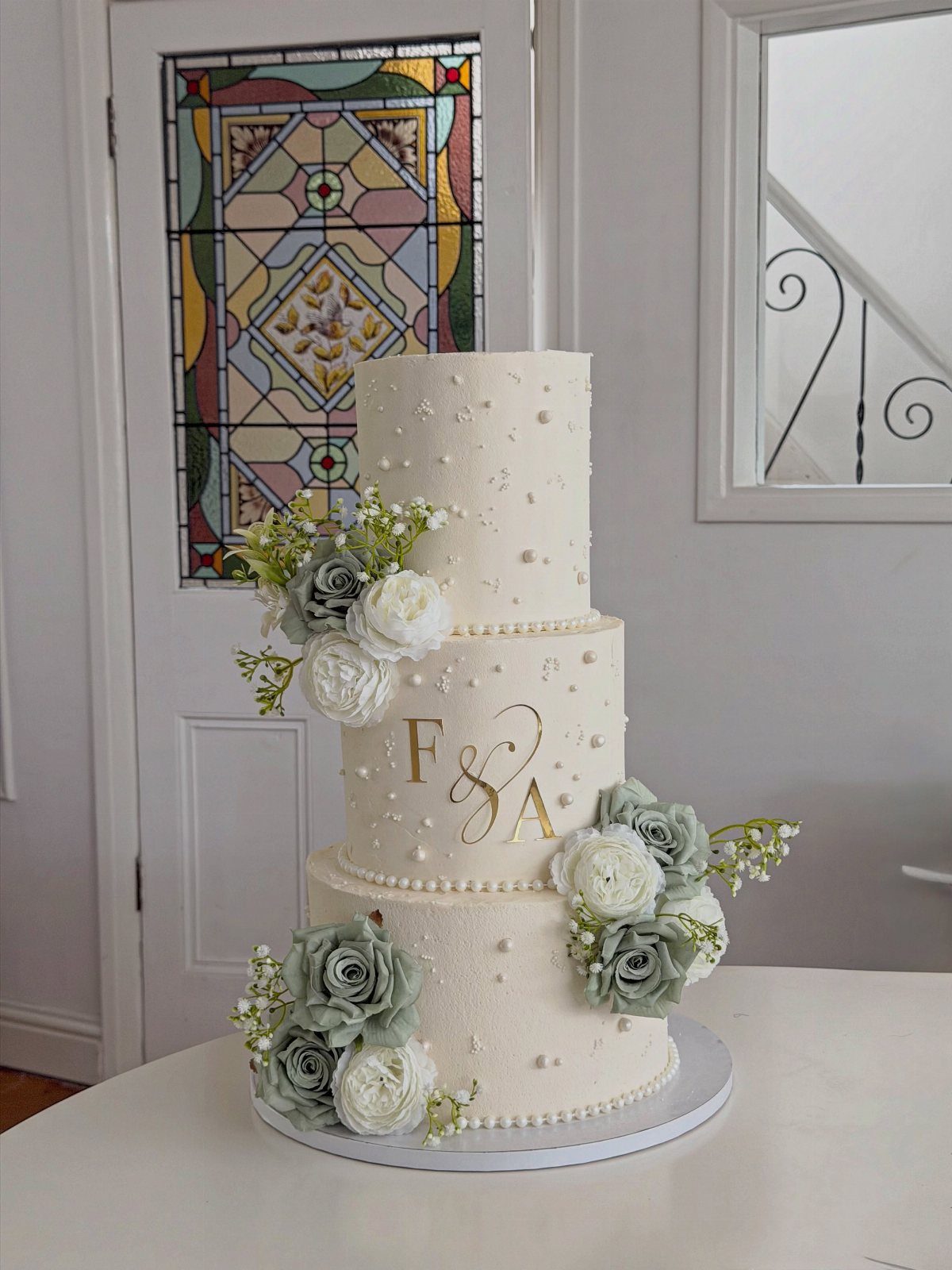 Wedding Detail Shots: 21 Ideas for Your Photographer 9 Three-tiered white wedding cake with gold initials and sage green floral decorations.