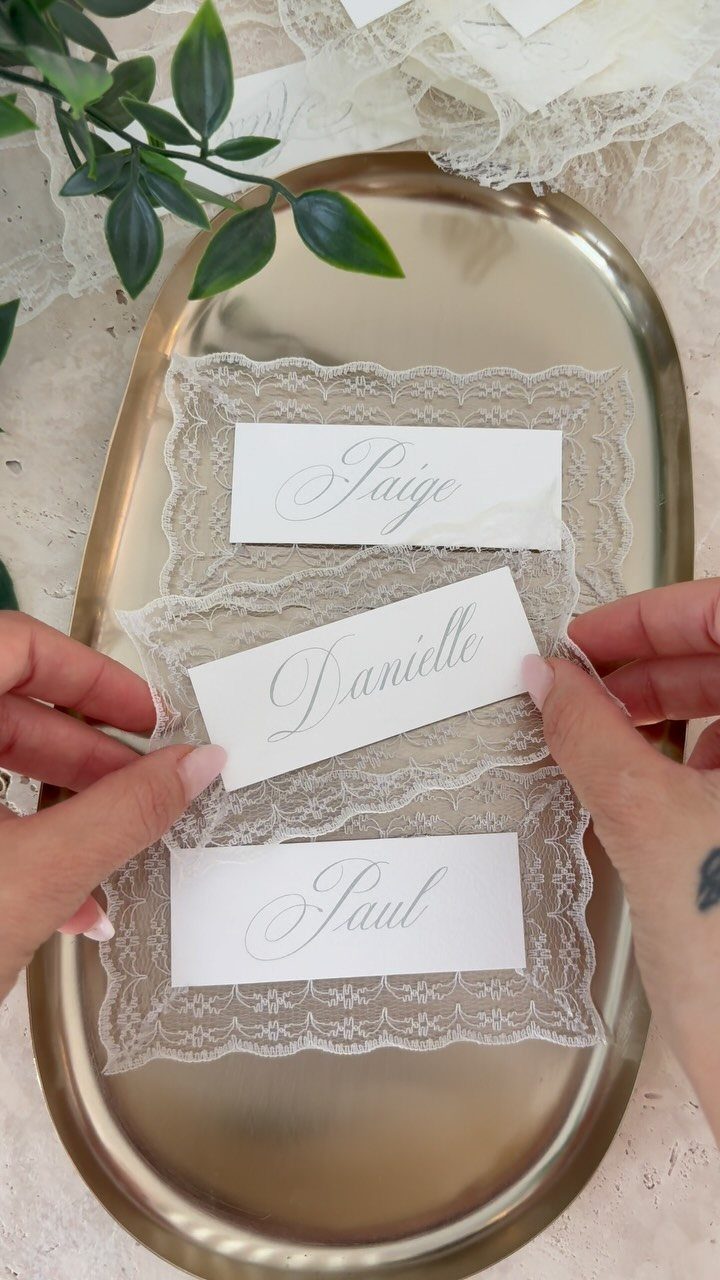 Wedding Detail Shots: 21 Ideas for Your Photographer 12 Hands holding white place cards with elegant script names over lace on a gold tray.