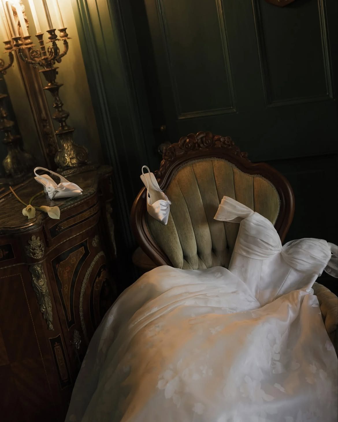 Wedding Detail Shots: 21 Ideas for Your Photographer 6 White wedding dress draped over a green velvet chair next to bridal shoes and an antique cabinet.
