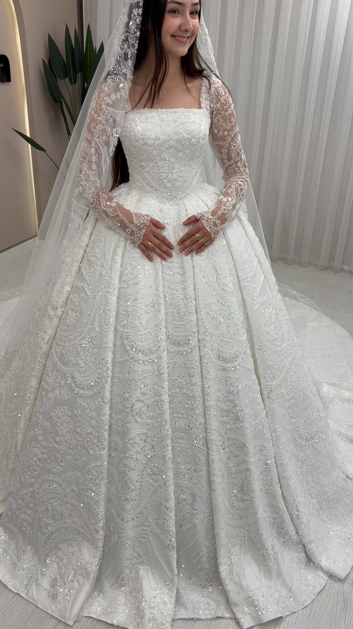 Woman in a white long-sleeved A-line wedding dress with intricate lace and sequins.