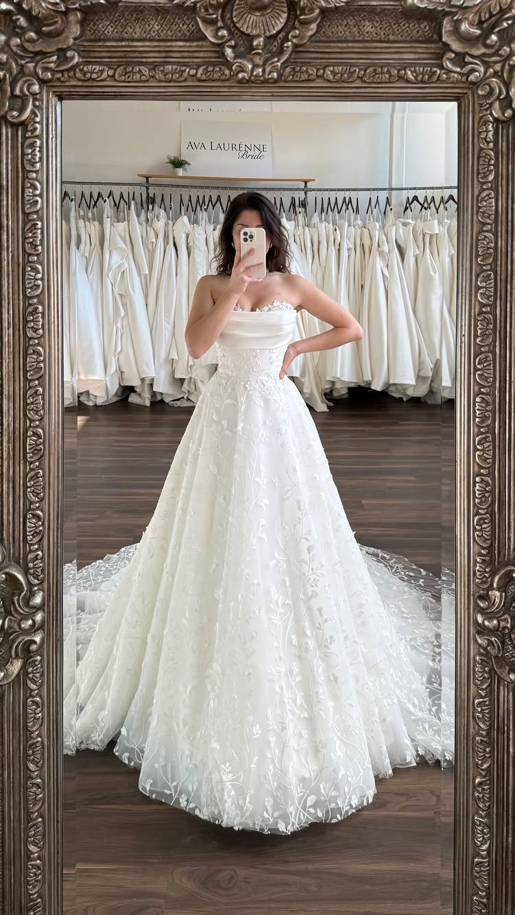 Woman in a strapless white lace A-line wedding dress posing in a mirror.