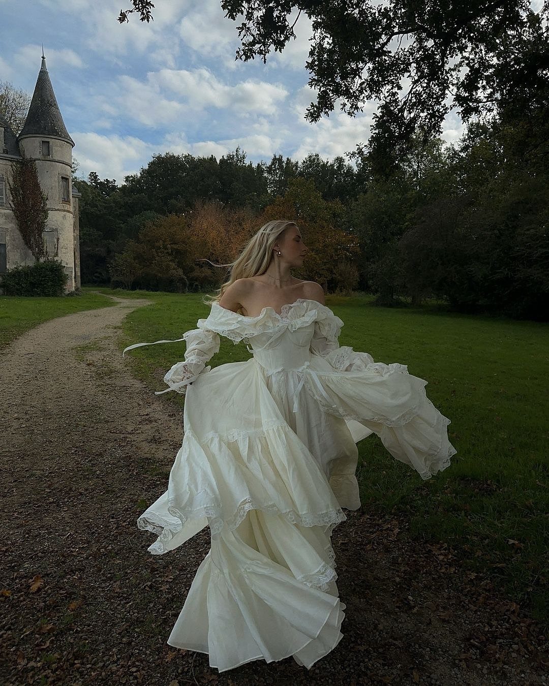 Woman in a voluminous white satin A-line wedding dress standing near a castle tower.