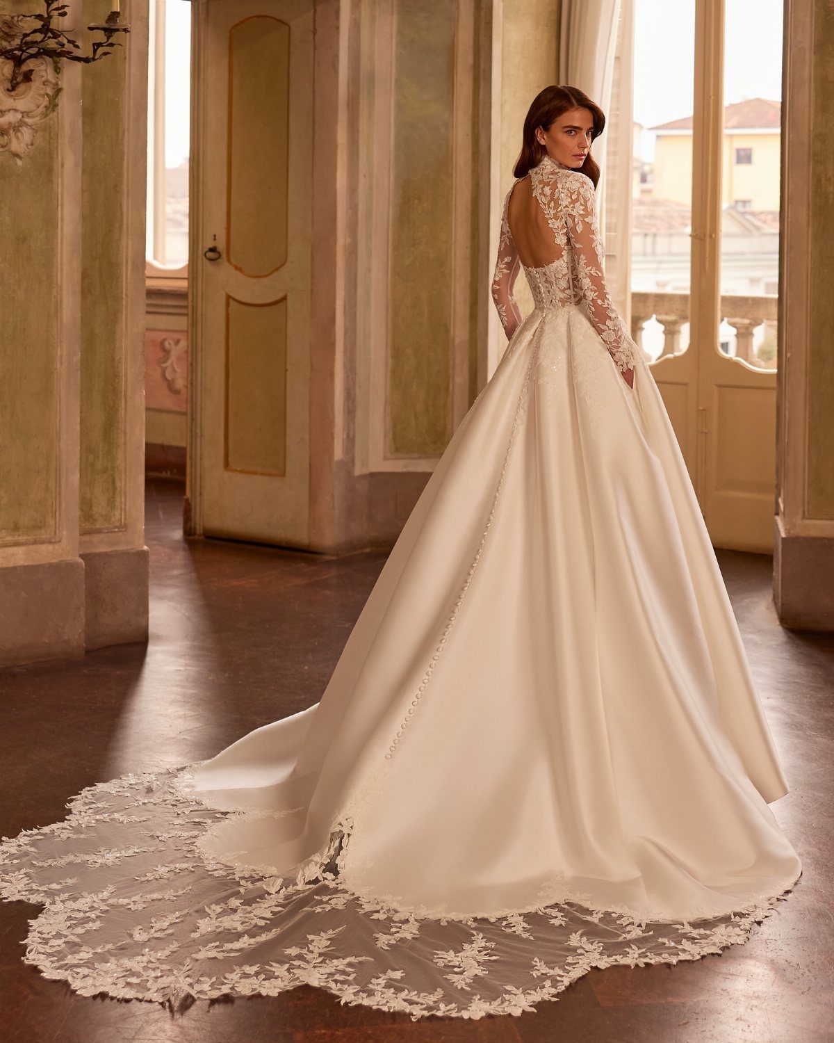 Woman in a white satin A-line wedding dress with long lace sleeves and train.