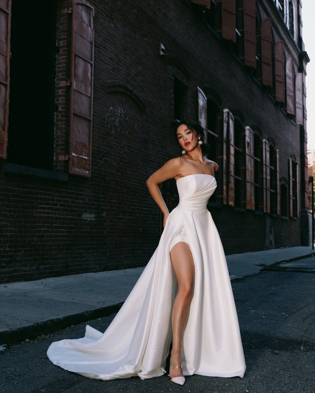 Woman in a strapless white satin A-line wedding dress with a high leg slit.