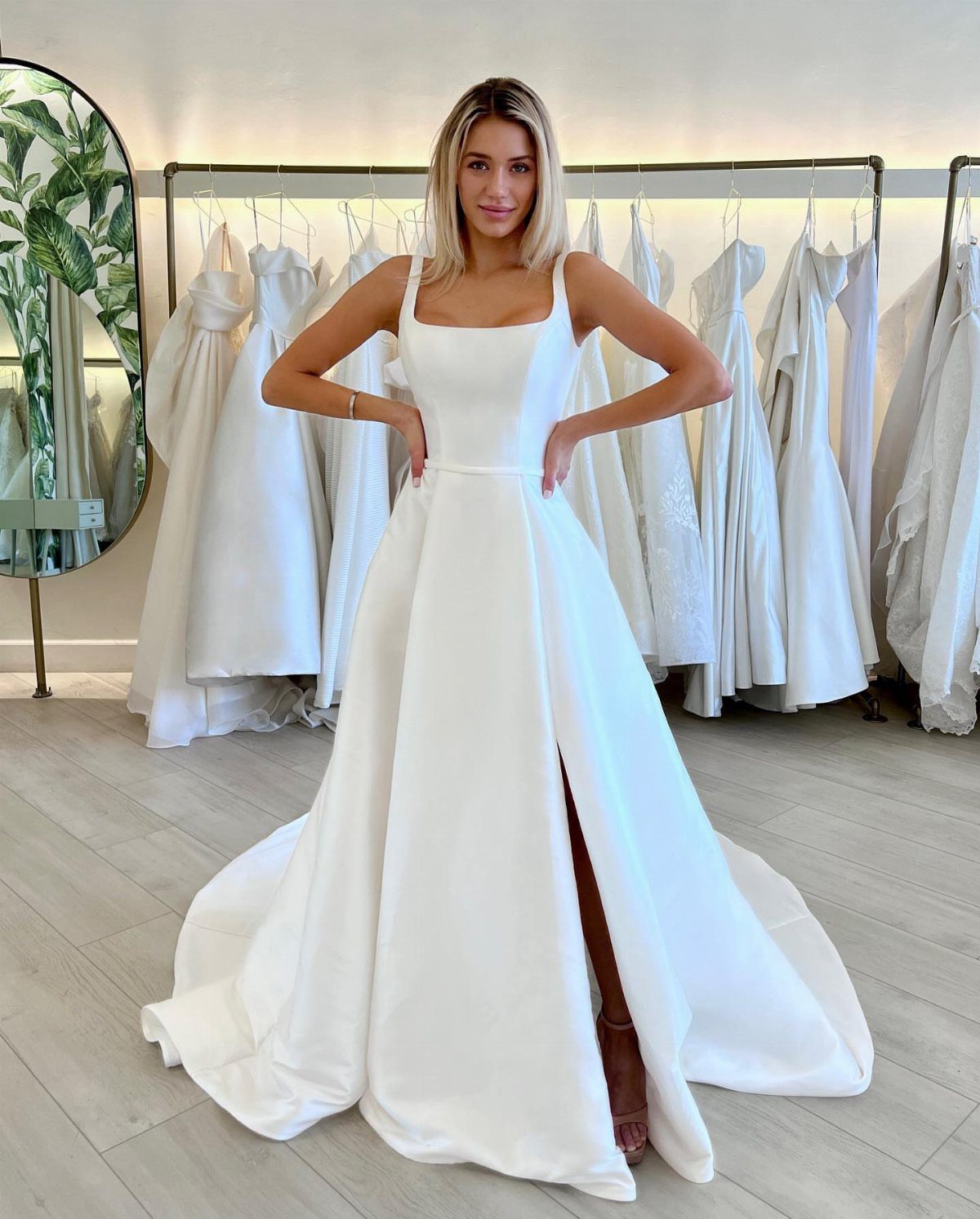 Woman in a white satin A-line wedding dress with a square neckline and leg slit.