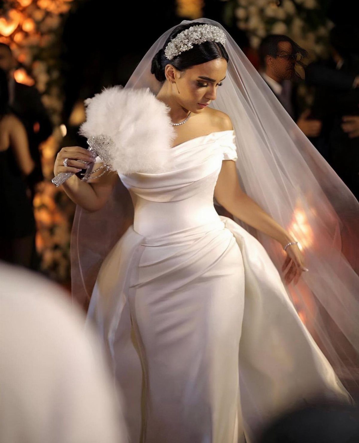 Woman in a white satin a-line wedding dress with a veil and tiara.