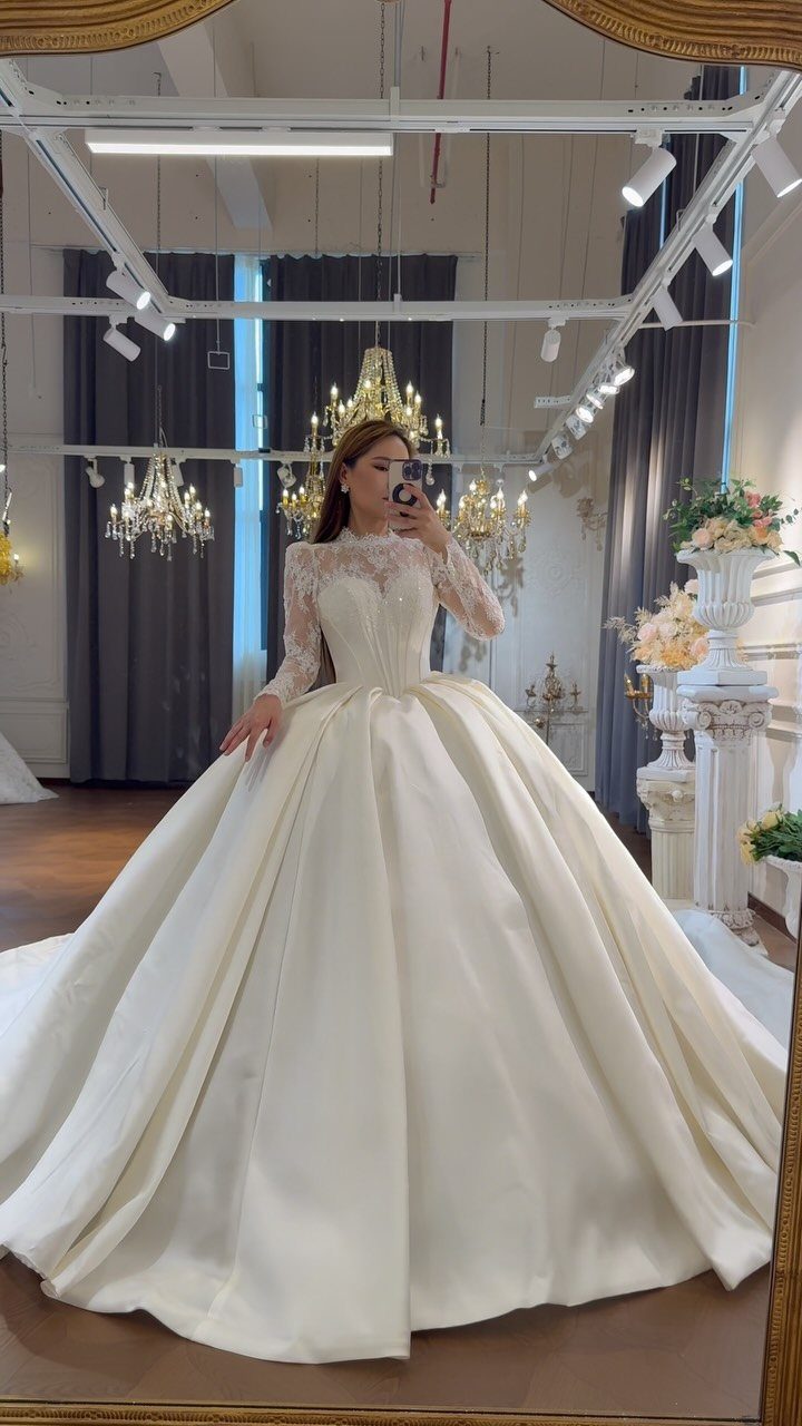 Woman wearing a white satin ball gown with a lace long-sleeved bodice.