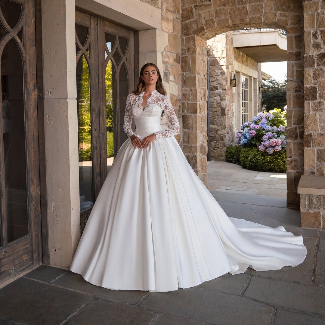 Woman in a white satin A-line wedding dress with lace sleeves on stone patio