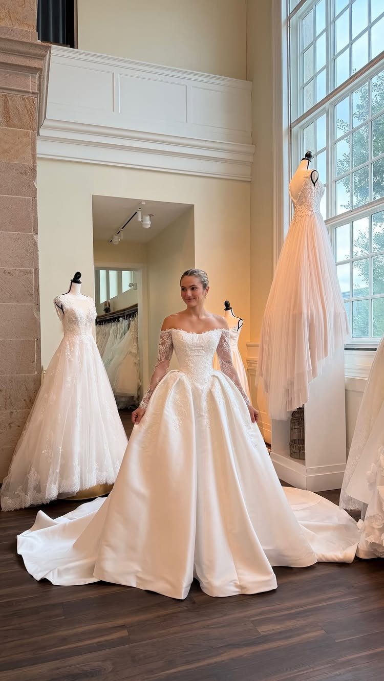 Woman in a white satin A-line wedding dress with lace sleeves in a boutique.