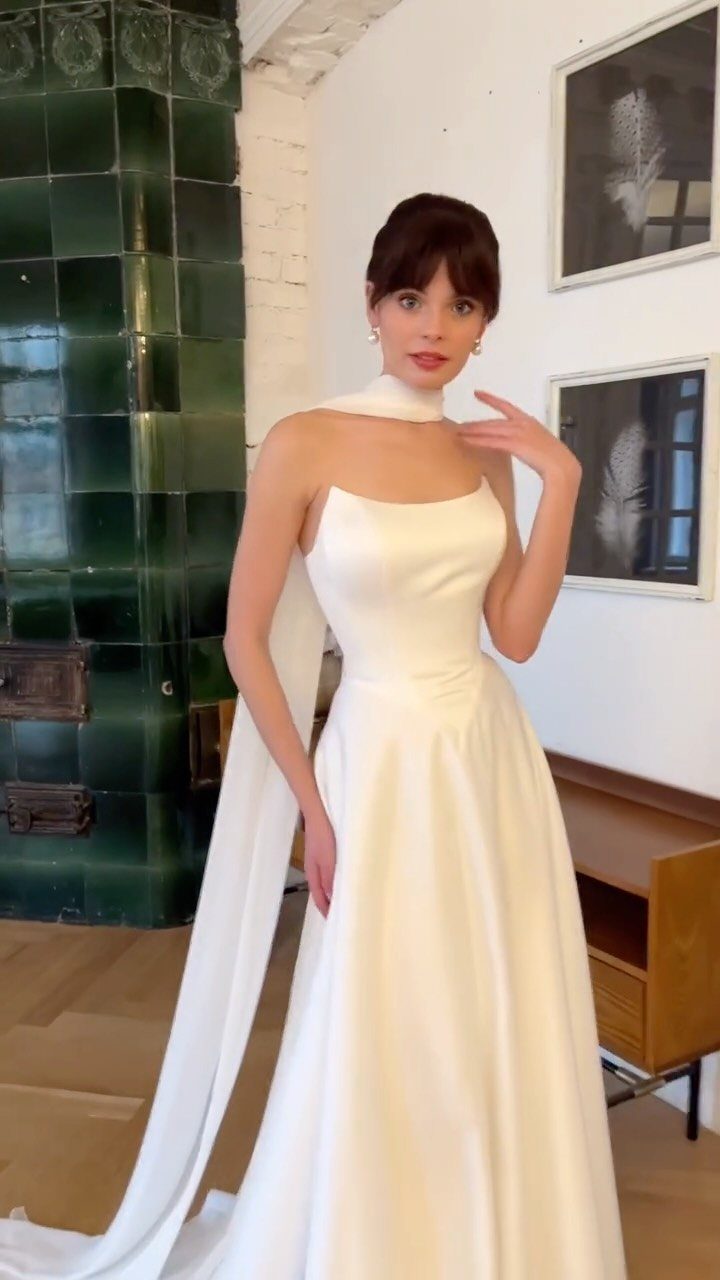 Woman in a white satin A-line wedding dress with a square neckline and long train.