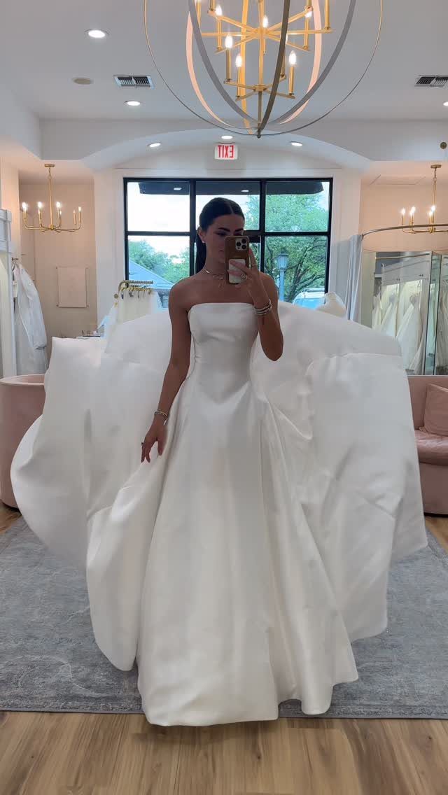 Woman in a strapless white satin A-line wedding dress posing in a bridal boutique.
