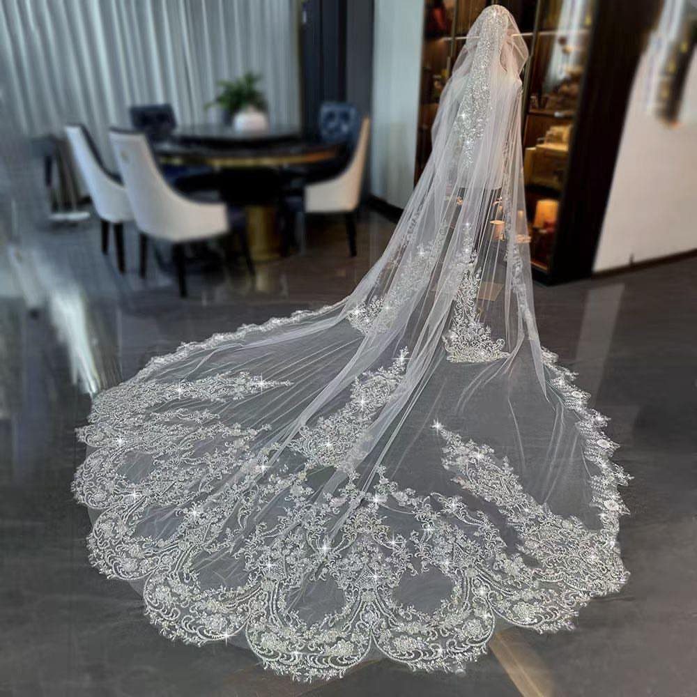 Long white cathedral wedding veil with detailed lace embroidery on a polished floor.