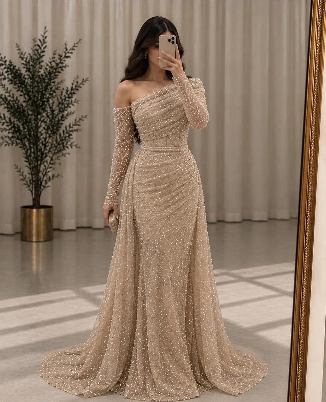 Woman in a shimmering champagne one-shoulder draped gown taking a mirror selfie.
