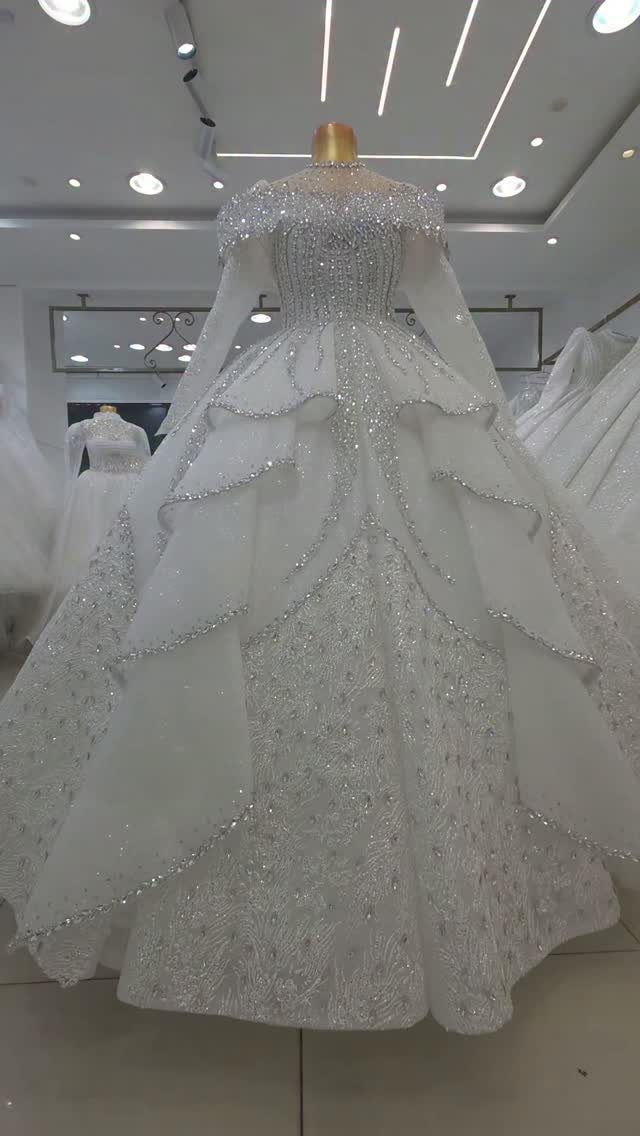 White floor-length wedding gown with long sleeves and shimmering tiered skirt on mannequin.