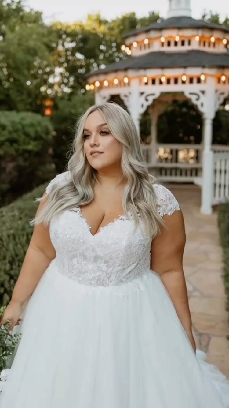 Woman in a white lace A-line wedding dress standing before a white gazebo.