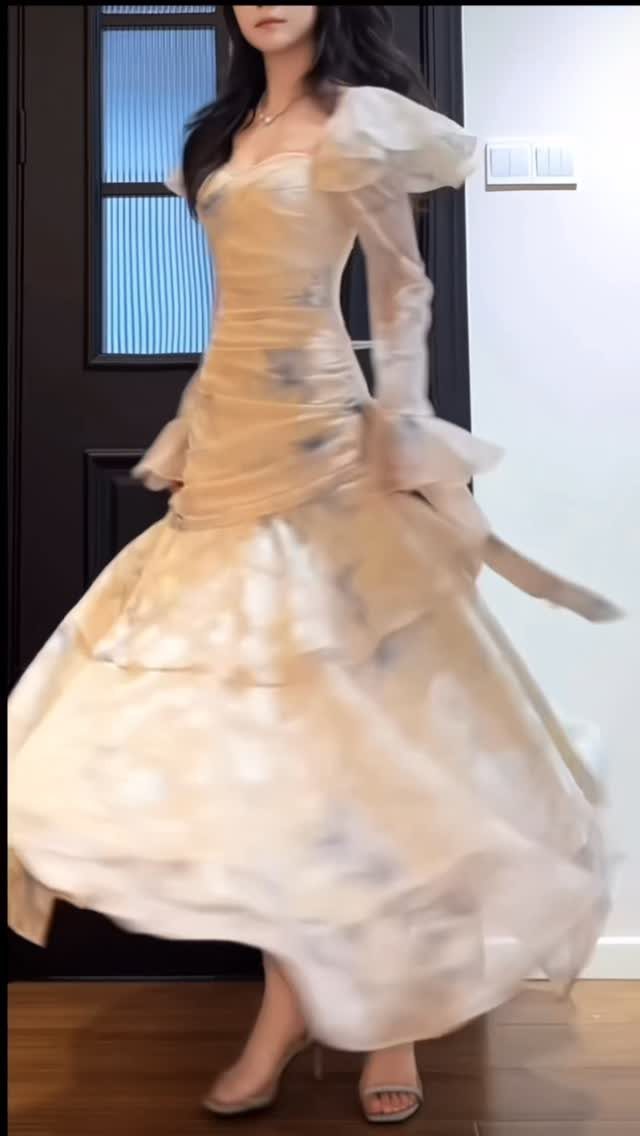 Woman in a long-sleeved champagne maxi gown with ruffled shoulders and full skirt.
