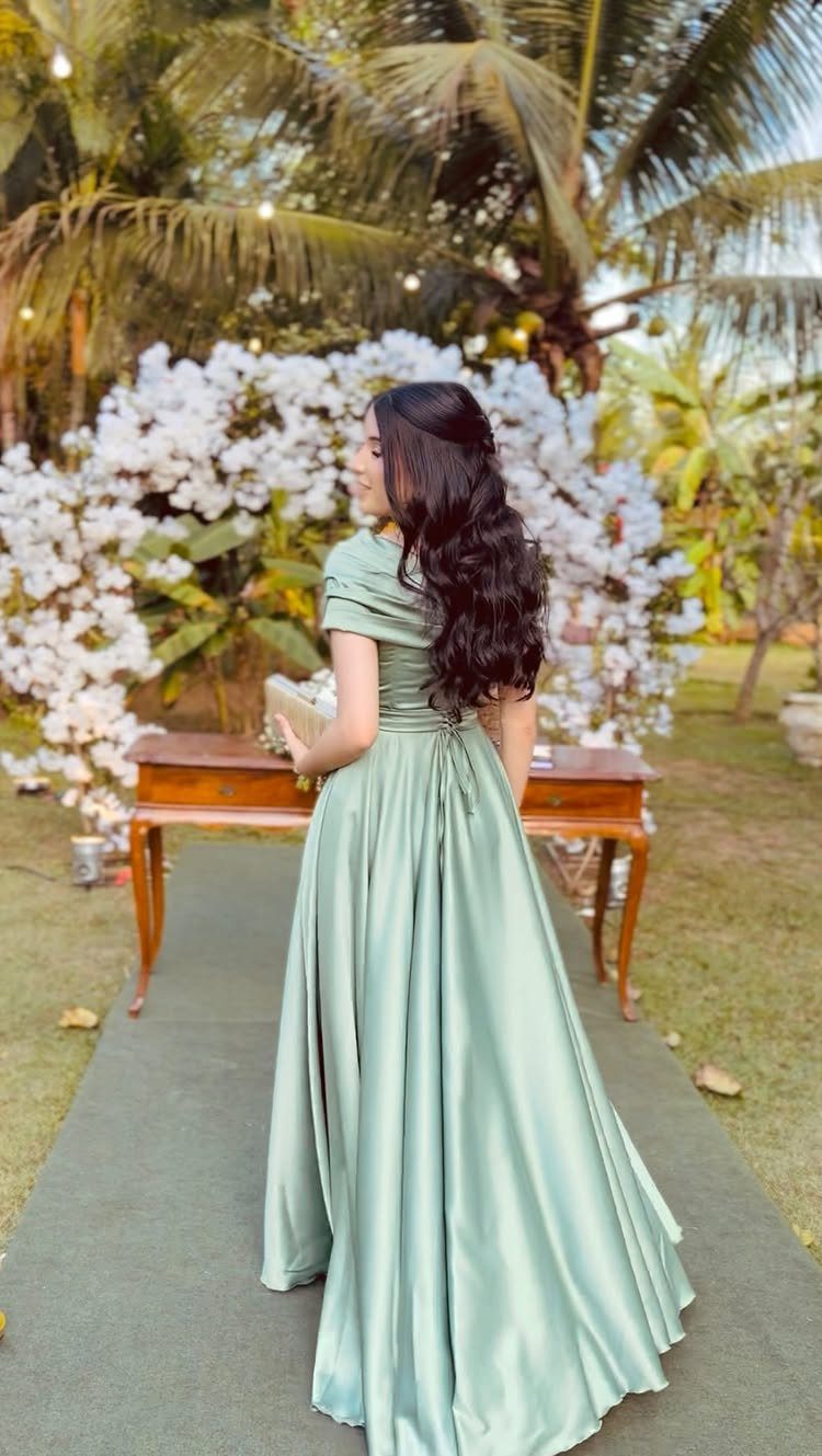 Woman in a sage green satin gown standing before white floral wedding decor.