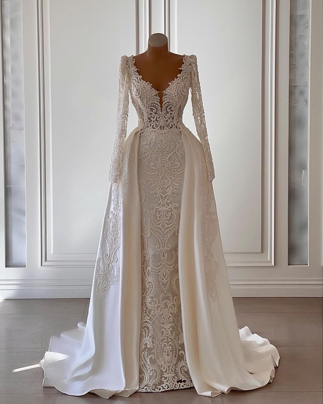 Tight Lace Wedding Dresses in 25 Beautiful Styles 26 Tight white lace wedding dress with long sleeves and a full overskirt on mannequin