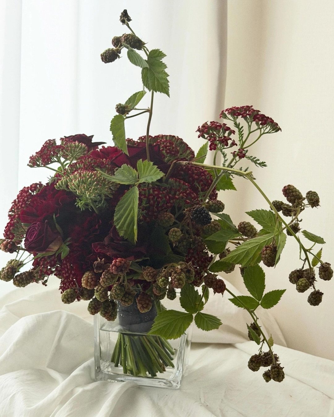 Wedding Flower Trends: 36 Ideas from Jewel Tones to Arches 37 Deep red roses and blackberries in a square glass vase on white fabric.