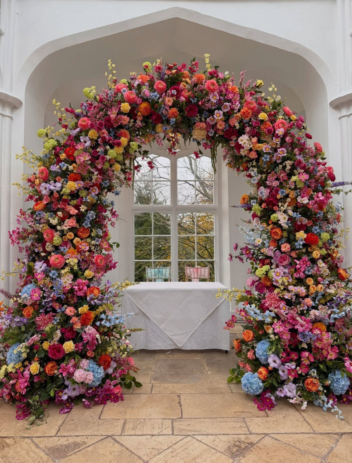 Wedding Flower Trends: 36 Ideas from Jewel Tones to Arches 29 Colorful floral arch with pink, red, and blue flowers framing a white table.