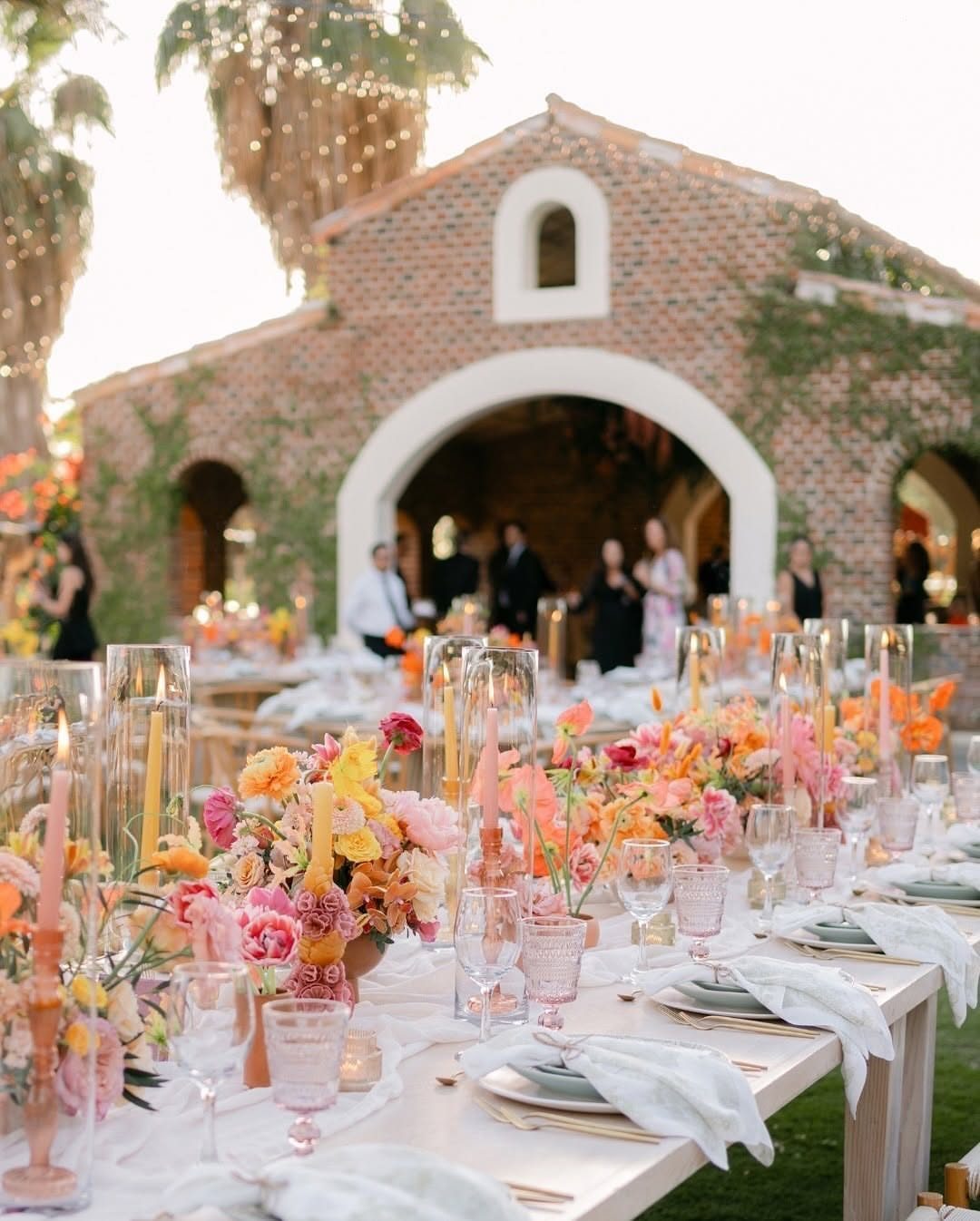 Wedding Flower Trends: 36 Ideas from Jewel Tones to Arches 14 Vibrant orange, yellow, and pink floral centerpieces on a white wedding reception table.