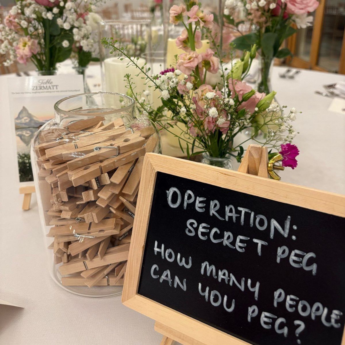 13 Wedding Games Table Ideas Your Guests Will Actually Play 13 A glass jar of wooden clothespins next to a chalkboard sign with game instructions.