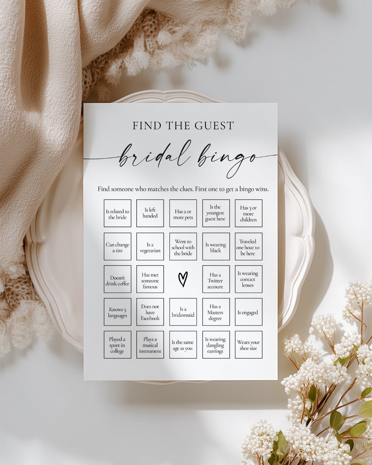 13 Wedding Games Table Ideas Your Guests Will Actually Play 5 A bridal bingo card with a grid of guest descriptions resting on a white plate.