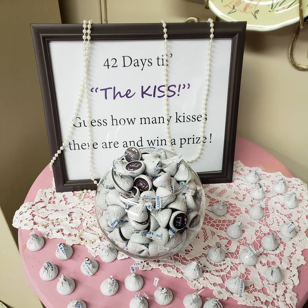 13 Wedding Games Table Ideas Your Guests Will Actually Play 12 A framed guessing game sign sits behind a glass bowl filled with Hershey's Kisses chocolates.