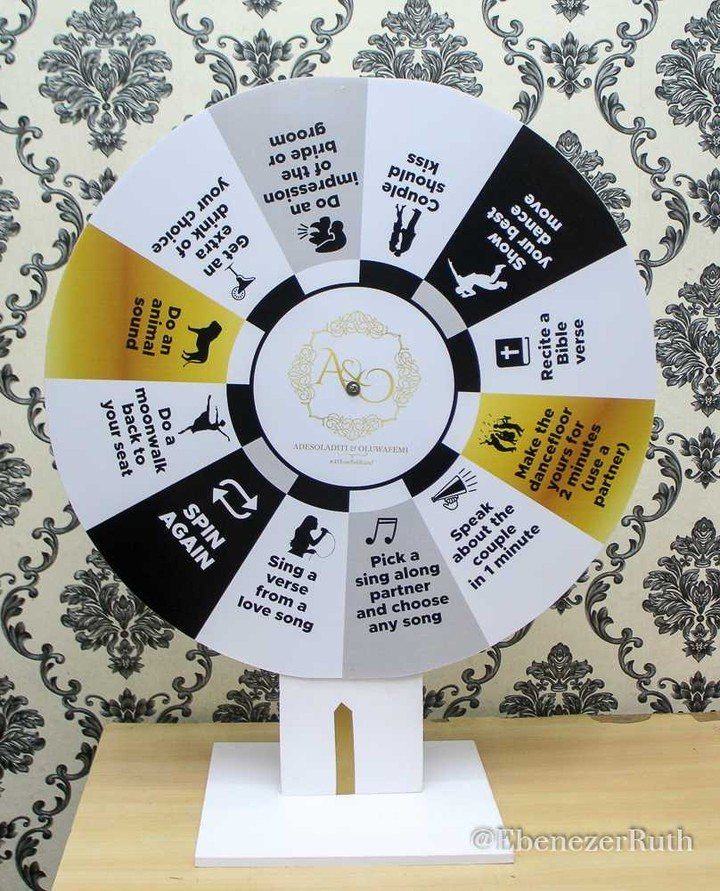 13 Wedding Games Table Ideas Your Guests Will Actually Play 7 A white spinning wheel with wedding game prompts on a patterned wallpaper background.