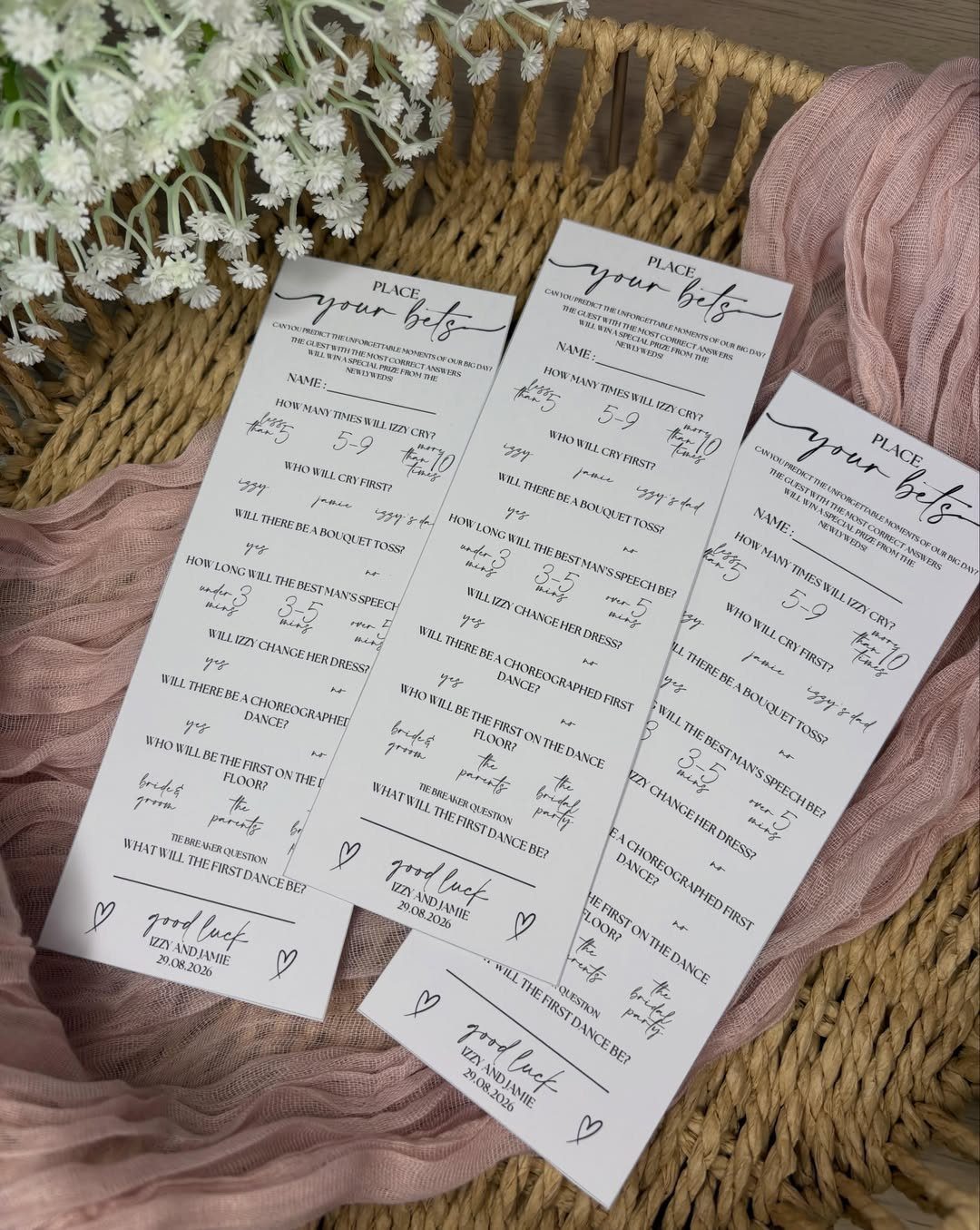 13 Wedding Games Table Ideas Your Guests Will Actually Play 11 Three white wedding betting cards resting in a wicker basket with pink fabric and white flowers.