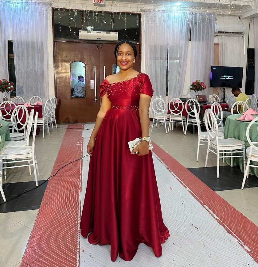 19 Wedding Guest Dress Ideas for Every Season and Style 13 Woman in a burgundy satin floor-length gown standing on a banquet hall runway.