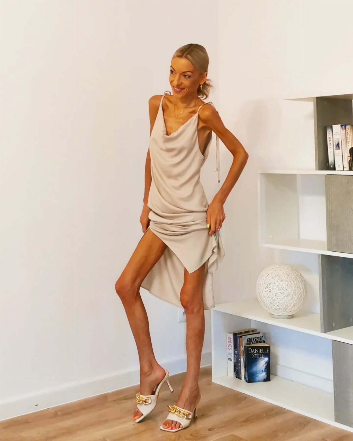 19 Wedding Guest Dress Ideas for Every Season and Style 11 Woman in a champagne satin cowl neck slip dress and white heeled sandals.