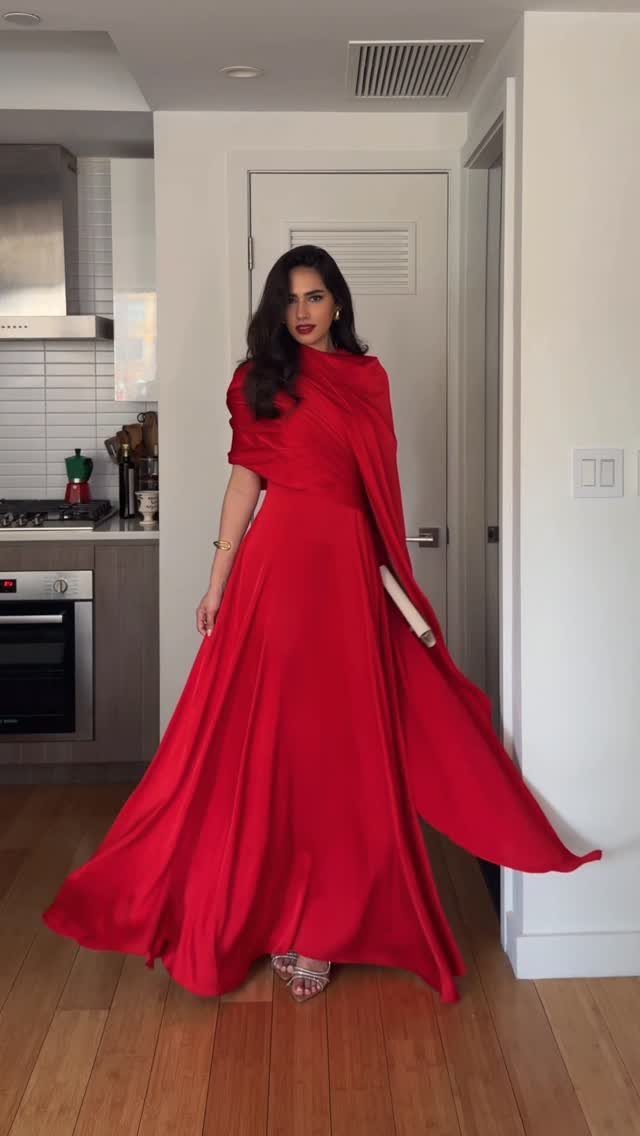 19 Wedding Guest Dress Ideas for Every Season and Style 17 Woman wearing a flowing floor-length red gown with a draped shoulder detail.