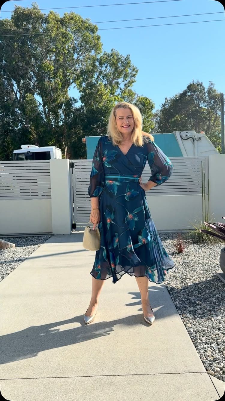 19 Wedding Guest Dress Ideas for Every Season and Style 6 Woman in navy blue floral midi wrap dress with silver heels and beige clutch.