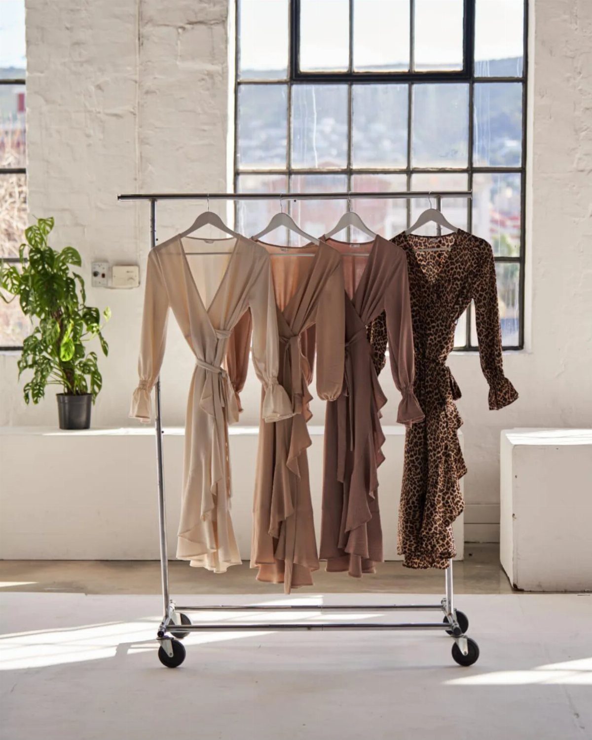 19 Wedding Guest Dress Ideas for Every Season and Style 10 Four wrap dresses with ruffled hems hanging on a silver garment rack.
