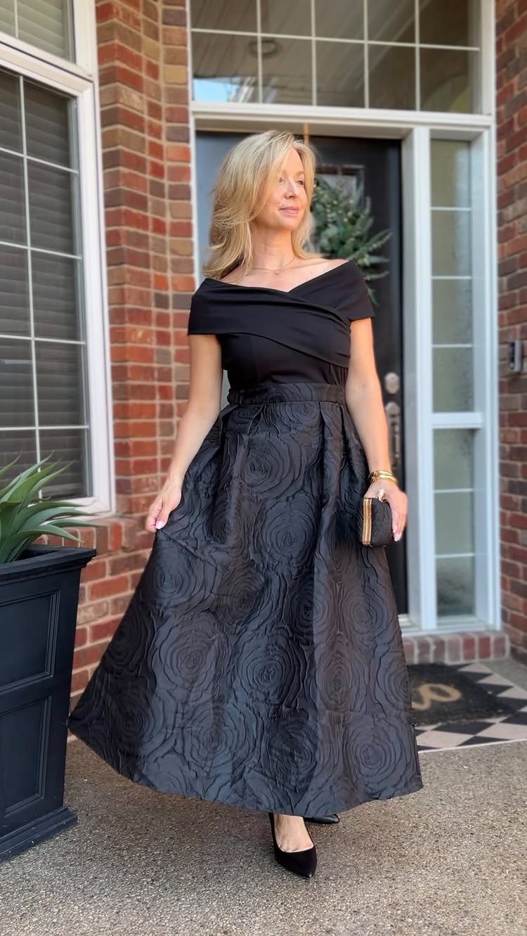 19 Wedding Guest Dress Ideas for Every Season and Style 15 Woman in a structured black top and full patterned maxi skirt standing outdoors.