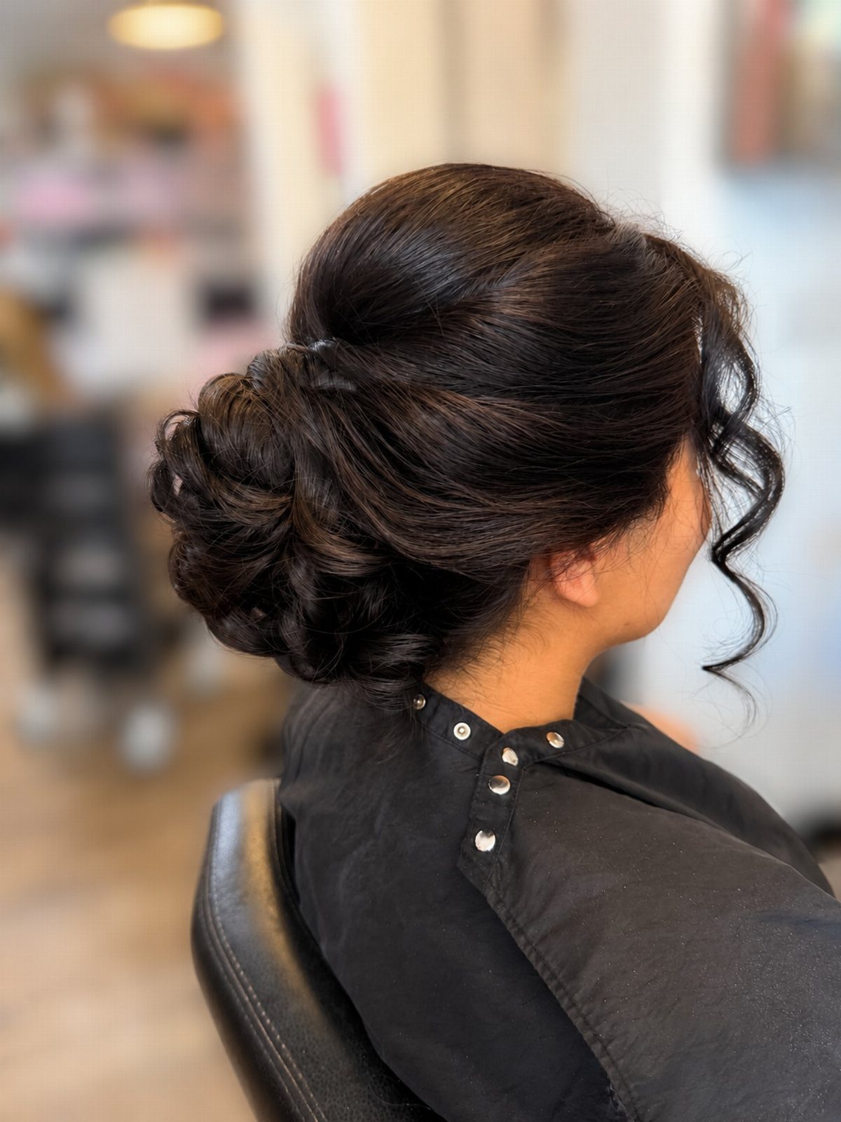 17 Wedding Guest Hairstyles Up: From Curled Updos to Bubble Braids 7 Woman with dark hair styled in a low textured updo with a face-framing curl.
