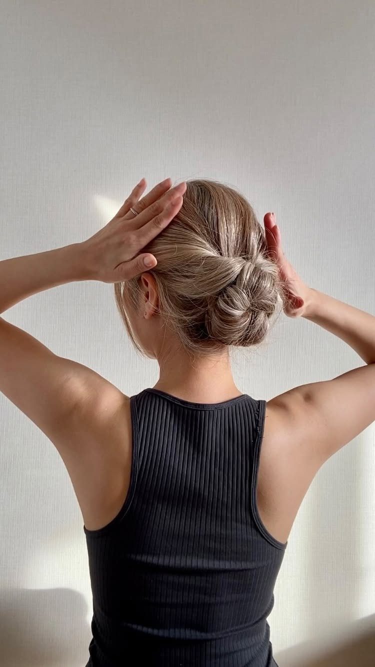 17 Wedding Guest Hairstyles Up: From Curled Updos to Bubble Braids 12 Blonde woman with hair styled in a low braided bun, seen from behind.