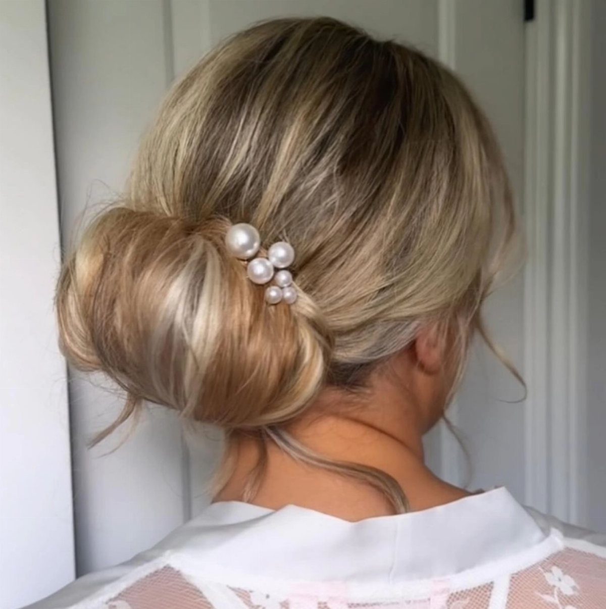 17 Wedding Guest Hairstyles Up: From Curled Updos to Bubble Braids 13 Blonde hair styled in a low bun decorated with large white pearls.