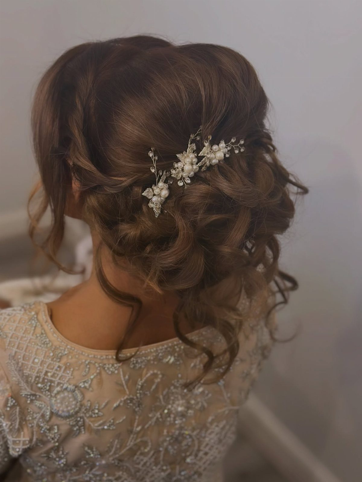 17 Wedding Guest Hairstyles Up: From Curled Updos to Bubble Braids 5 A woman's brown hair styled in a textured updo with a floral hair accessory.