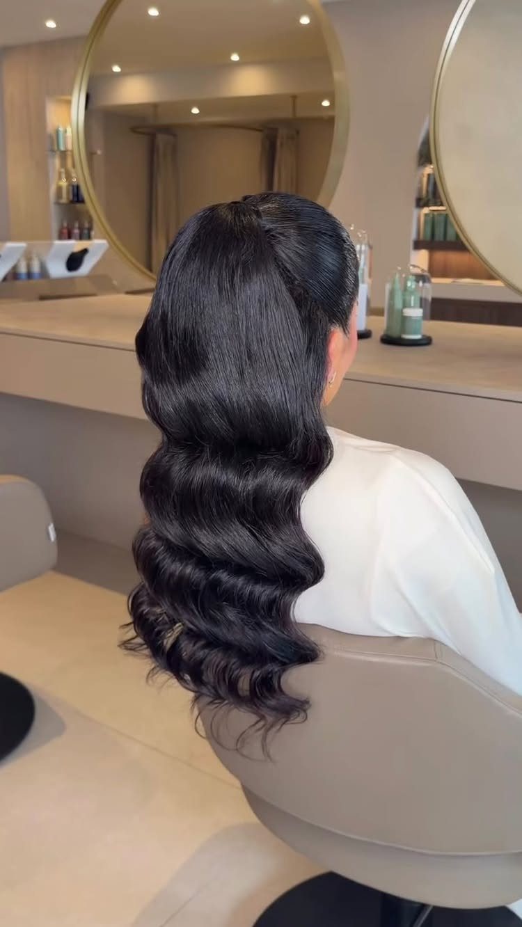 Long dark hair styled in deep structured waves seen from behind in a salon.