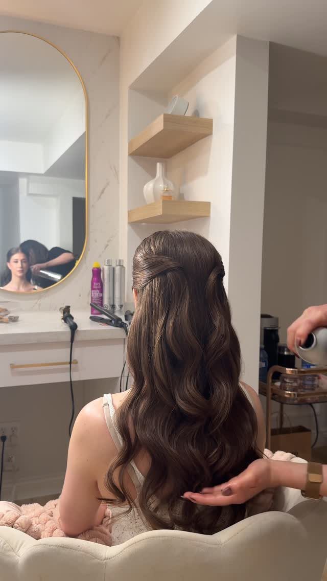 Woman with long brown wavy hair styled in a half-up, half-down wedding hairstyle.